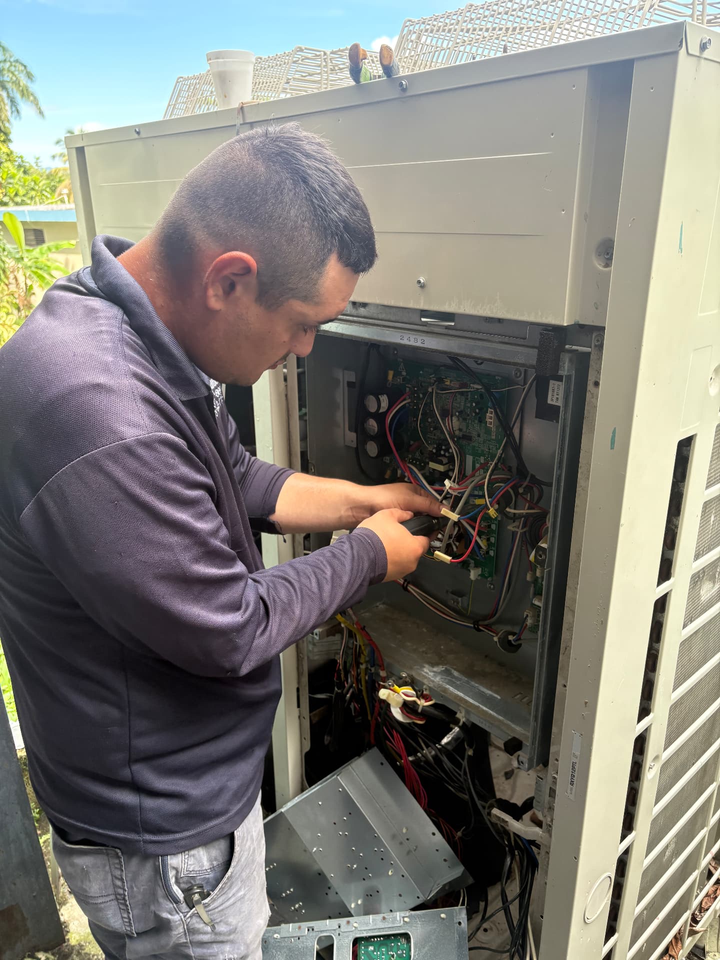 Técnico de JL trabajando en el cableado de un equipo condensador de aire acondicionado abierto al aire libre