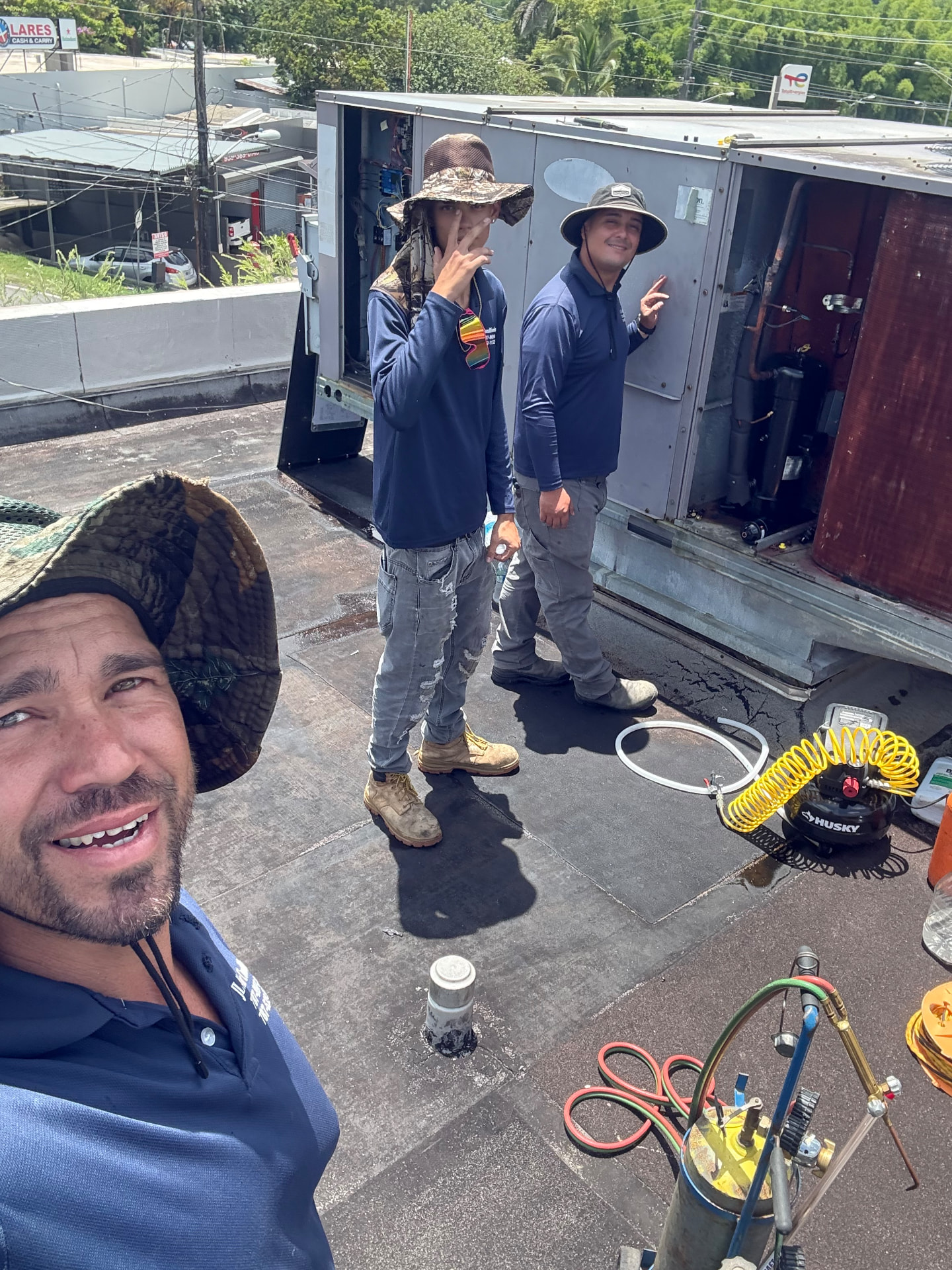 Tres técnicos de JL junto a un equipo rooftop abierto en azotea, con herramientas de soldadura a un lado